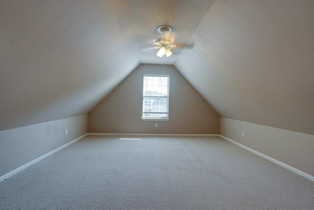 additional living space with baseboards, ceiling fan, carpet, vaulted ceiling, and a textured ceiling