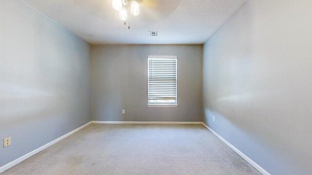 unfurnished room featuring a ceiling fan, light colored carpet, visible vents, and baseboards