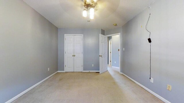 unfurnished bedroom with a closet, light colored carpet, ceiling fan, and baseboards