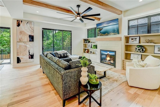 2207 W 71st St, Prairie Village, KS 66208 - living room featuring wood finished floors, plenty of natural light, a ceiling fan, a glass covered fireplace, and beam ceiling