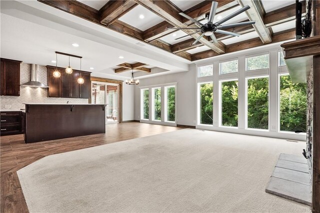 interior space with beamed ceiling, coffered ceiling, wall chimney exhaust hood, pendant lighting, and decorative backsplash