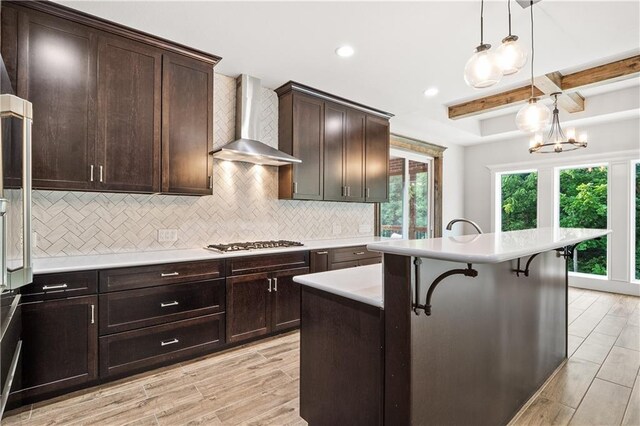 kitchen with light wood-type flooring, wall chimney exhaust hood, an island with sink, a breakfast bar area, and tasteful backsplash