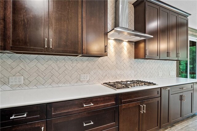 kitchen with backsplash, stainless steel gas cooktop, dark brown cabinets, and wall chimney exhaust hood