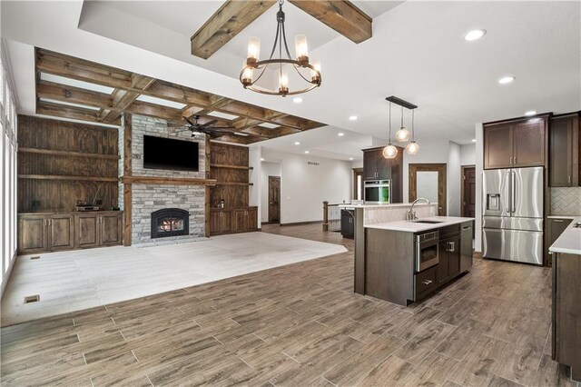 kitchen featuring a fireplace, ceiling fan with notable chandelier, appliances with stainless steel finishes, sink, and a kitchen island with sink