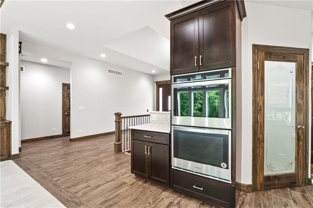 kitchen featuring dark brown cabinets, light hardwood / wood-style floors, and stainless steel double oven