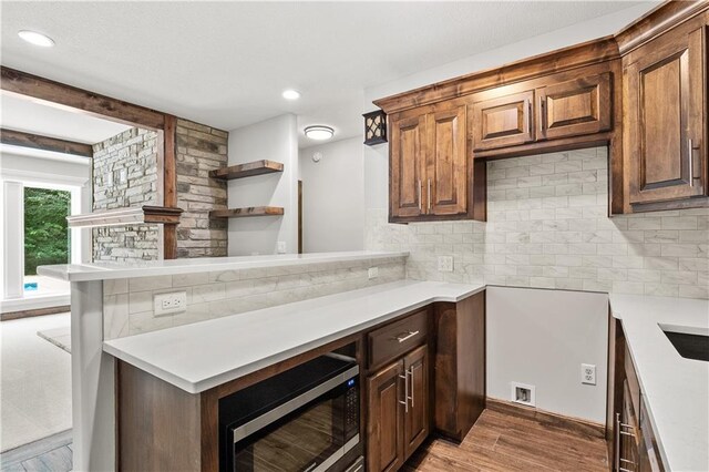 kitchen with stainless steel microwave, beamed ceiling, hardwood / wood-style floors, and decorative backsplash