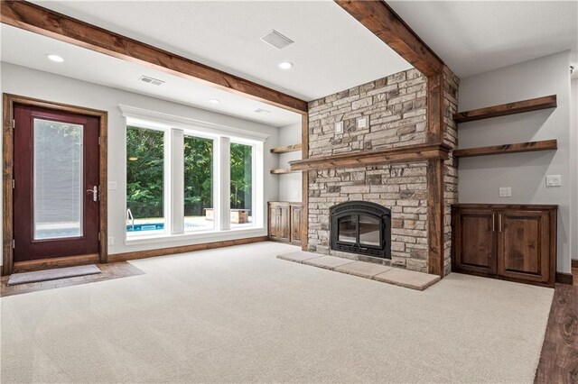 unfurnished living room featuring a stone fireplace, beam ceiling, and light carpet