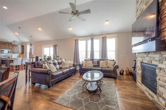 living room featuring ceiling fan, a stone fireplace, dark wood-type flooring, and lofted ceiling