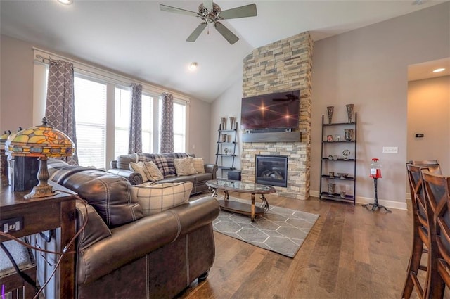 living room featuring hardwood / wood-style flooring, ceiling fan, vaulted ceiling, and a stone fireplace