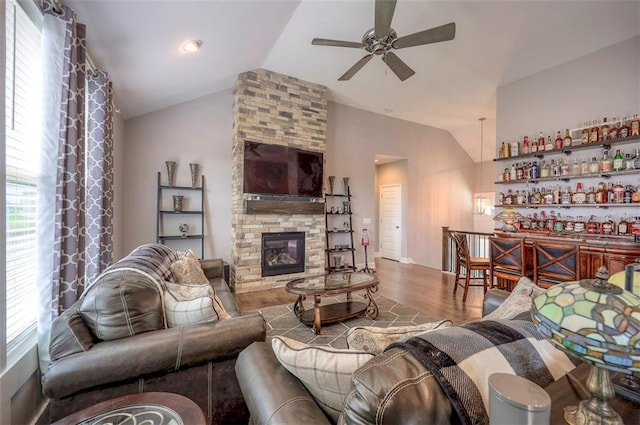 living room with ceiling fan, hardwood / wood-style flooring, a stone fireplace, and lofted ceiling