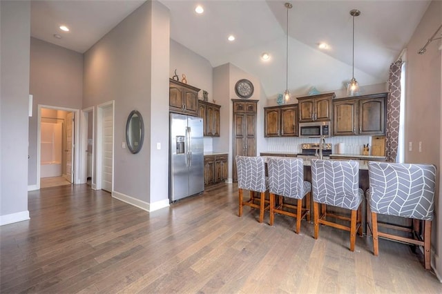 kitchen with stainless steel appliances, light hardwood / wood-style floors, decorative backsplash, decorative light fixtures, and a kitchen breakfast bar