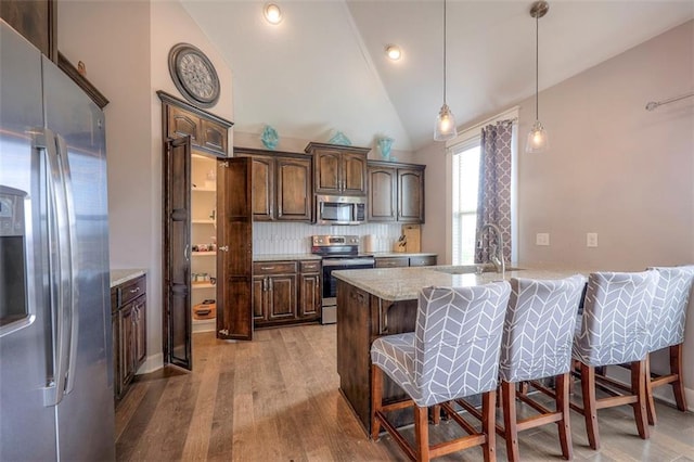 kitchen with stainless steel appliances, light hardwood / wood-style floors, dark brown cabinets, tasteful backsplash, and a breakfast bar area