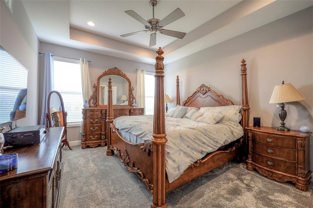 bedroom featuring a tray ceiling, ceiling fan, multiple windows, and light carpet