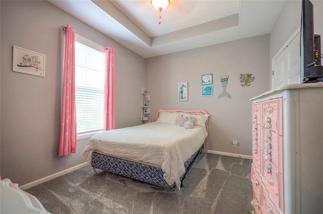 bedroom featuring ceiling fan, dark carpet, and a raised ceiling