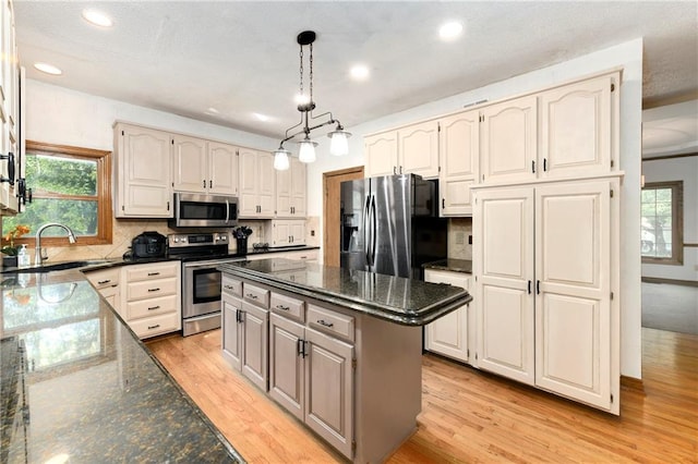 kitchen featuring backsplash, dark stone countertops, a center island, light wood-type flooring, and appliances with stainless steel finishes