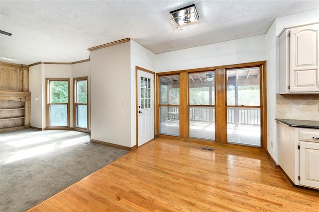 interior space featuring ornamental molding, a textured ceiling, and light wood-type flooring