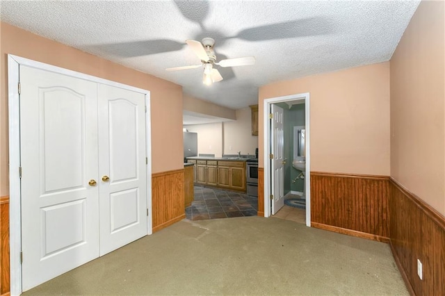 interior space with ceiling fan, a textured ceiling, carpet flooring, connected bathroom, and a closet