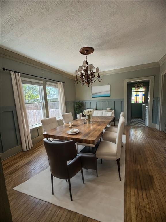 dining room with hardwood / wood-style flooring, a textured ceiling, an inviting chandelier, crown molding, and a decorative wall