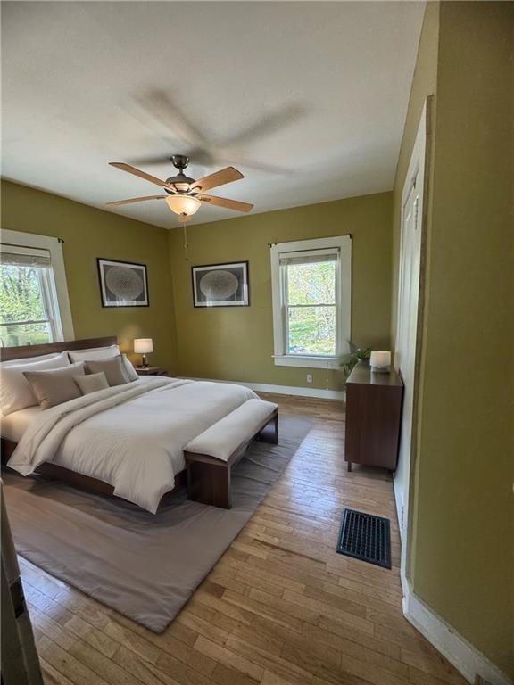 bedroom featuring multiple windows, a ceiling fan, baseboards, and wood finished floors