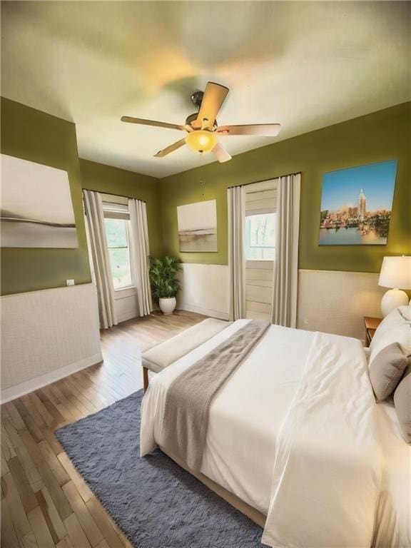 bedroom featuring a ceiling fan, wood finished floors, and wainscoting