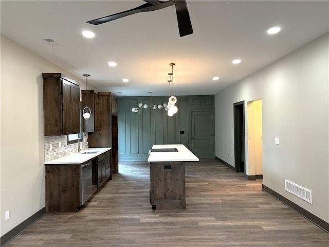 kitchen with pendant lighting, sink, backsplash, dark brown cabinets, and a kitchen island