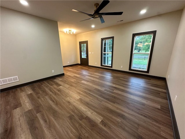 empty room featuring ceiling fan, a healthy amount of sunlight, and dark hardwood / wood-style flooring