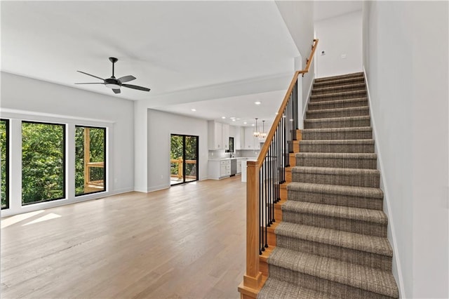 staircase with hardwood / wood-style flooring and ceiling fan with notable chandelier