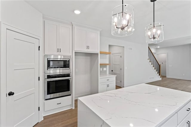 kitchen with hanging light fixtures, white cabinets, stainless steel appliances, wood-type flooring, and a notable chandelier