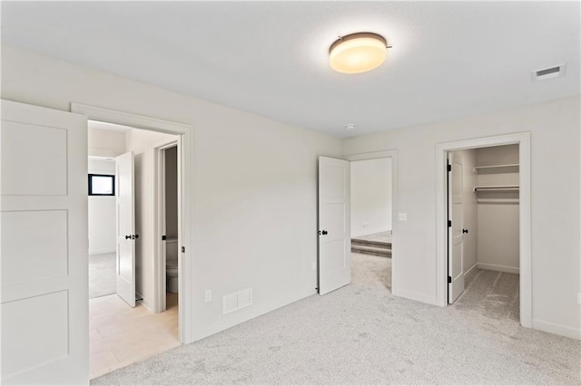 unfurnished bedroom featuring a closet, a spacious closet, light colored carpet, and ensuite bath