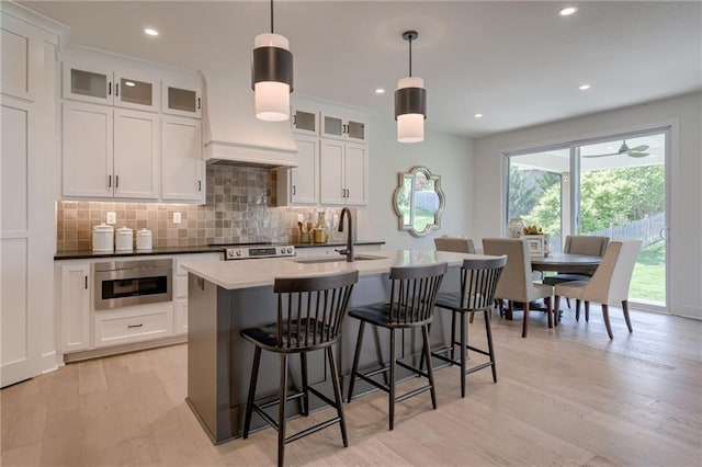 4805 NE 62nd St, Kansas City, MO 64119 - kitchen with backsplash, light wood-type flooring, a kitchen island with sink, a kitchen bar, and white cabinets