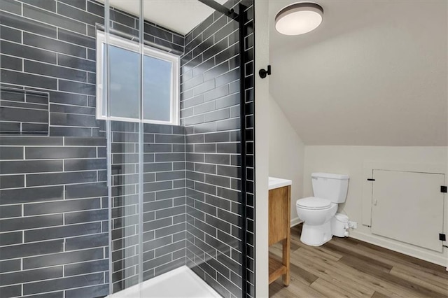 bathroom with lofted ceiling, a tile shower, hardwood / wood-style flooring, toilet, and vanity