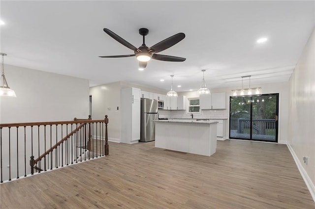 kitchen with light wood finished floors, a kitchen island, stainless steel appliances, white cabinetry, and tasteful backsplash