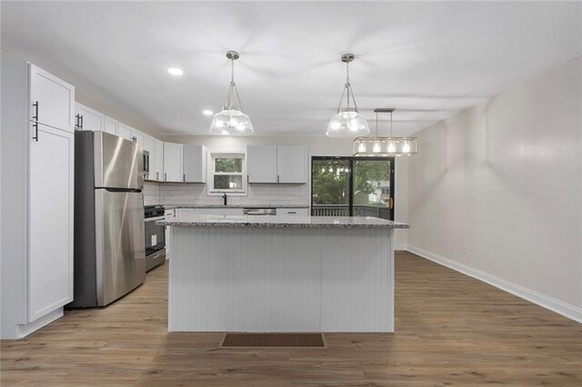 kitchen featuring pendant lighting, appliances with stainless steel finishes, light hardwood / wood-style floors, backsplash, and white cabinetry