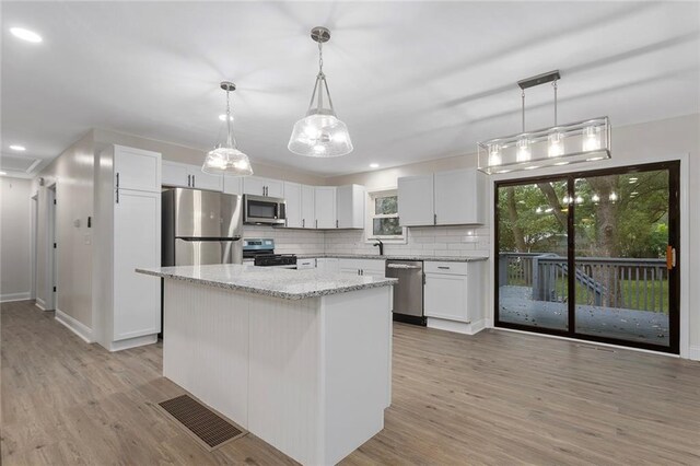 kitchen with appliances with stainless steel finishes, light wood-type flooring, pendant lighting, and decorative backsplash