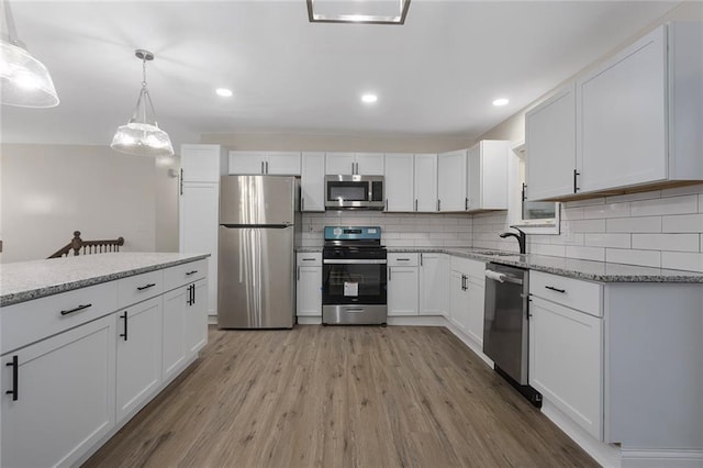 kitchen with light wood-style flooring, light stone counters, white cabinetry, stainless steel appliances, and decorative backsplash