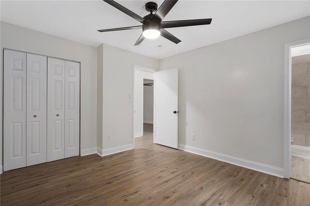 unfurnished bedroom featuring ceiling fan, a closet, wood-type flooring, and connected bathroom