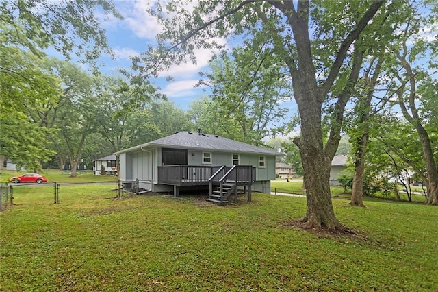 rear view of property featuring a shingled roof, a lawn, a deck, and fence