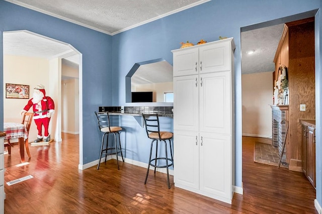 kitchen with hardwood / wood-style floors, a kitchen bar, crown molding, a textured ceiling, and white cabinets