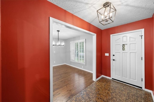 foyer entrance featuring an inviting chandelier, a textured ceiling, and dark hardwood / wood-style floors