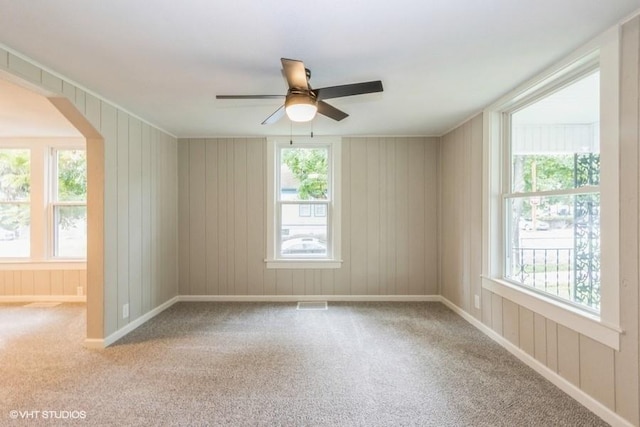 carpeted spare room featuring arched walkways, a healthy amount of sunlight, ceiling fan, and visible vents