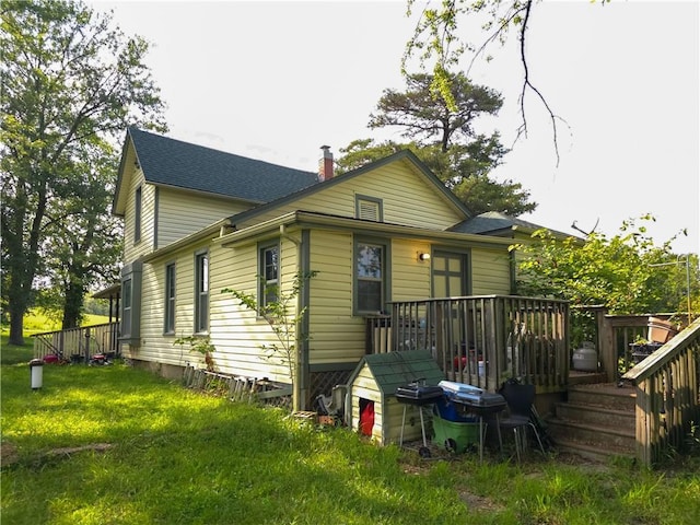 back of property featuring a shingled roof, a lawn, a chimney, and a wooden deck