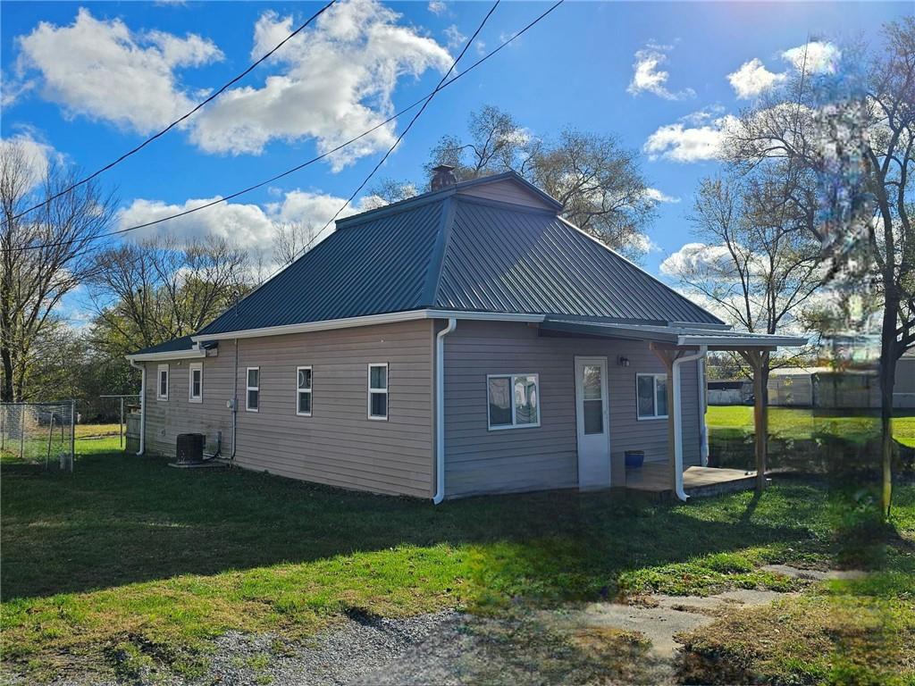 view of side of property featuring a chimney, a lawn, metal roof, fence, and cooling unit