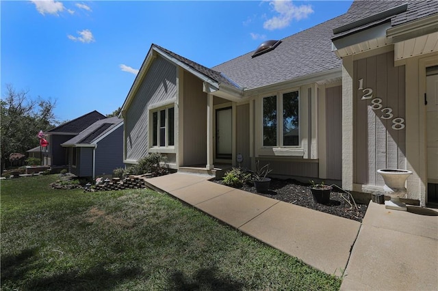 view of exterior entry featuring a lawn and roof with shingles