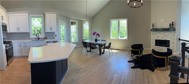 kitchen with white cabinetry, light hardwood / wood-style floors, sink, a fireplace, and lofted ceiling