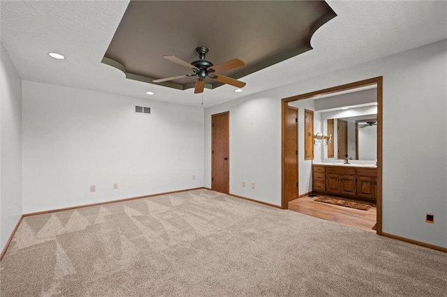 unfurnished bedroom featuring sink, a tray ceiling, light colored carpet, and ensuite bathroom