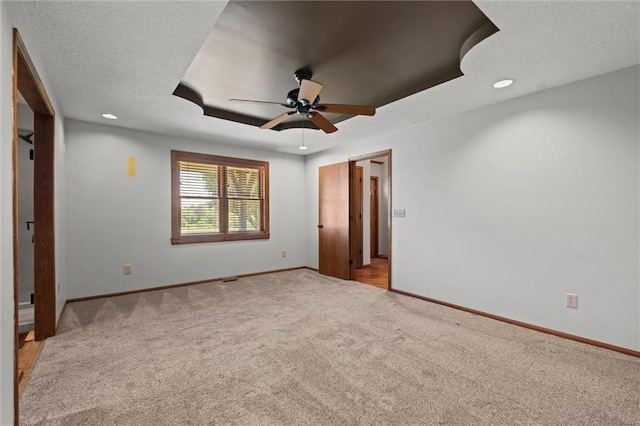 unfurnished bedroom featuring a tray ceiling, light colored carpet, ceiling fan, and a textured ceiling