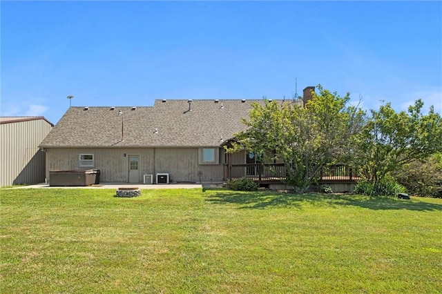 back of house featuring a wooden deck, a yard, a hot tub, and a fire pit