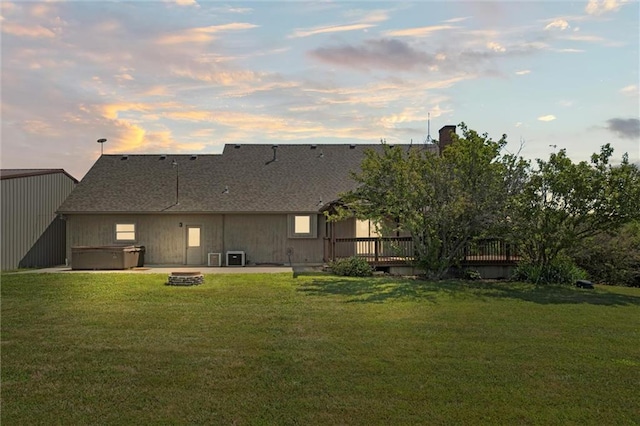 back house at dusk featuring a deck, a hot tub, a lawn, and an outdoor fire pit