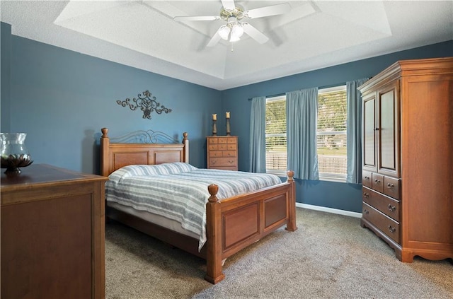 bedroom featuring baseboards, a tray ceiling, ceiling fan, and light colored carpet