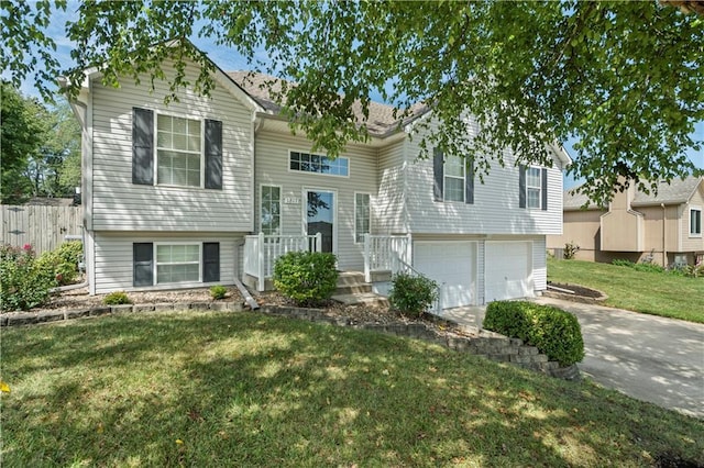 raised ranch featuring a front yard, driveway, an attached garage, and fence